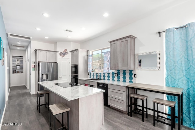 kitchen featuring gray cabinetry, a sink, a kitchen breakfast bar, black appliances, and tasteful backsplash