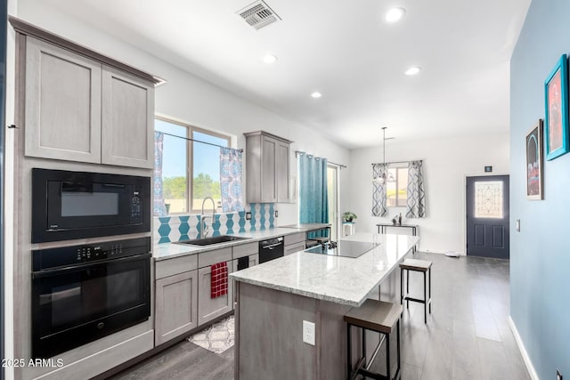 kitchen with a center island, gray cabinets, visible vents, a sink, and black appliances