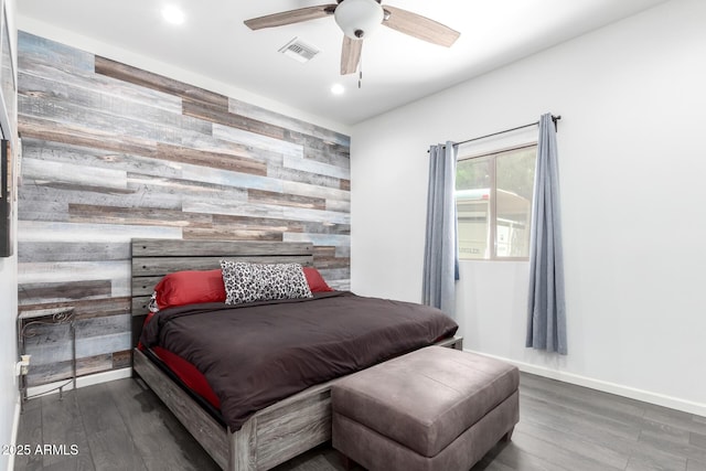 bedroom featuring an accent wall, wood walls, wood finished floors, visible vents, and baseboards