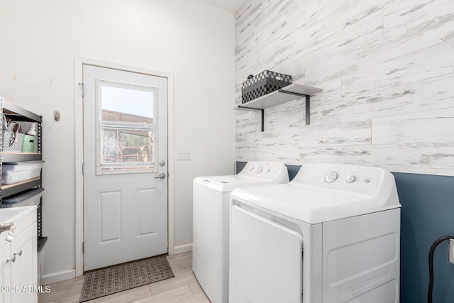 clothes washing area featuring an accent wall, washing machine and dryer, cabinet space, and baseboards