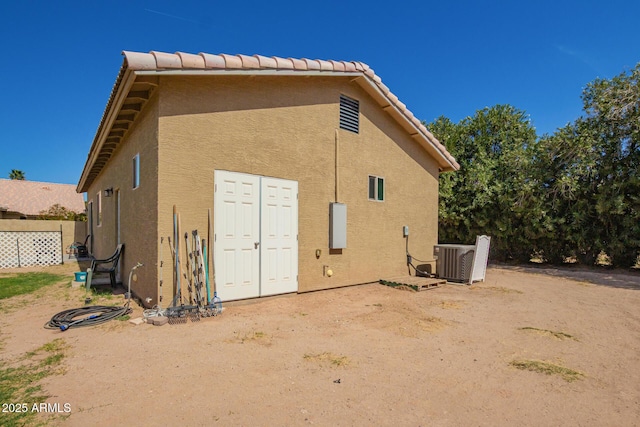 rear view of house with cooling unit, a tile roof, and stucco siding