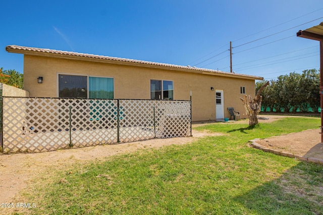 back of house featuring a lawn, a tiled roof, and stucco siding