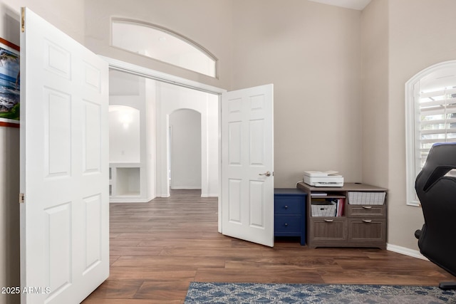 office space with arched walkways, a high ceiling, dark wood-style floors, and baseboards