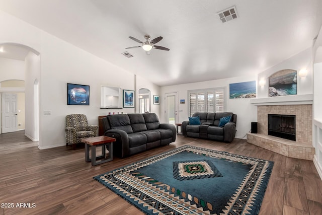 living room featuring lofted ceiling, visible vents, a fireplace with raised hearth, and wood finished floors