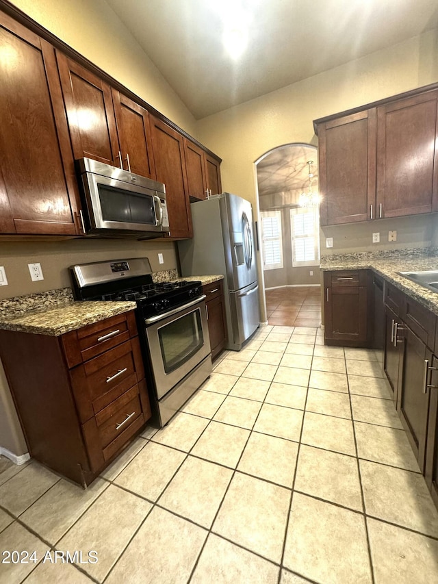 kitchen featuring appliances with stainless steel finishes, dark brown cabinetry, light tile patterned floors, dark stone countertops, and lofted ceiling