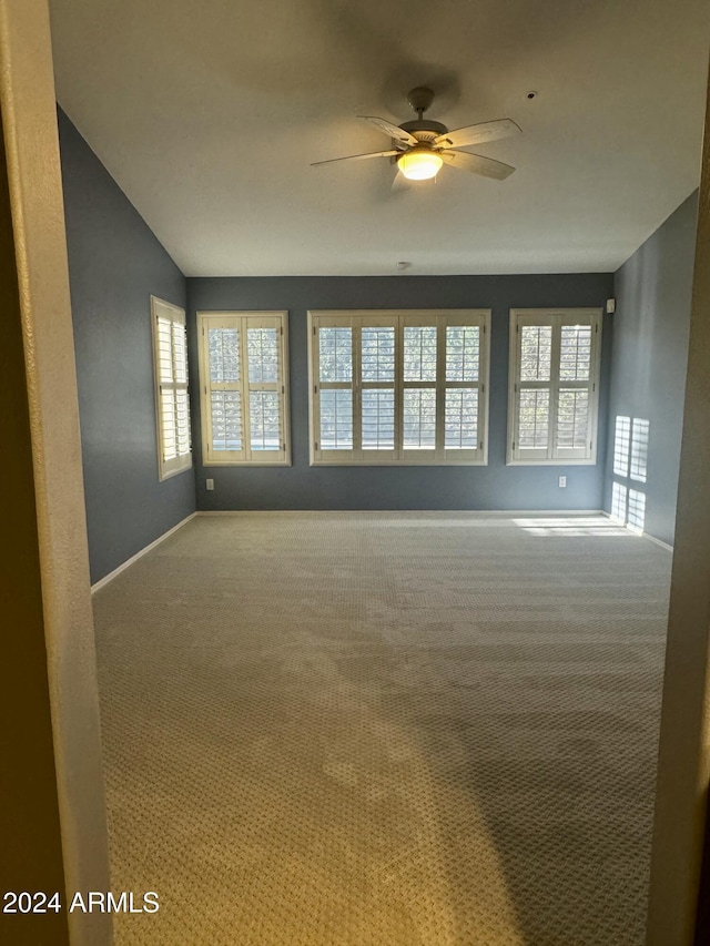 carpeted spare room with ceiling fan, a healthy amount of sunlight, and lofted ceiling