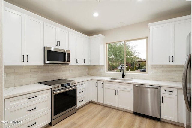 kitchen featuring stainless steel appliances, white cabinets, light wood-type flooring, and tasteful backsplash