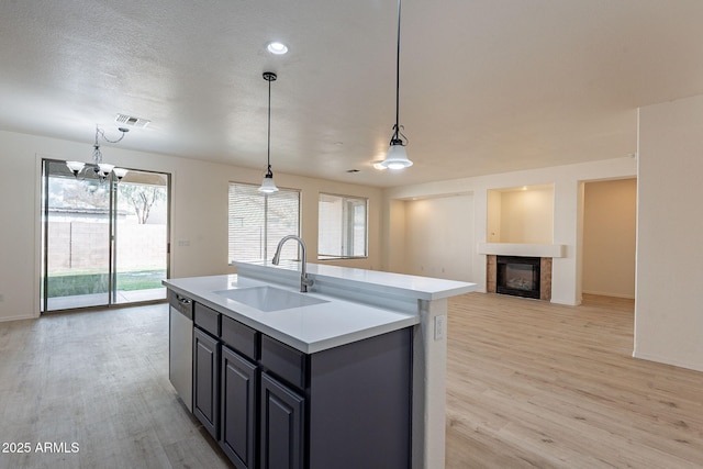 kitchen with sink, hanging light fixtures, light hardwood / wood-style flooring, dishwasher, and a kitchen island with sink