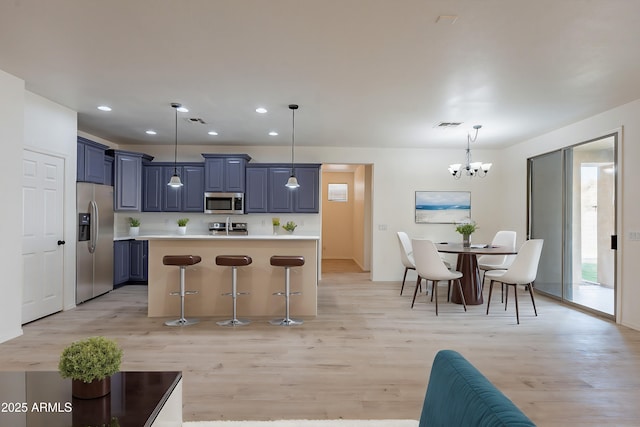 kitchen featuring a breakfast bar, stainless steel appliances, blue cabinetry, pendant lighting, and a notable chandelier