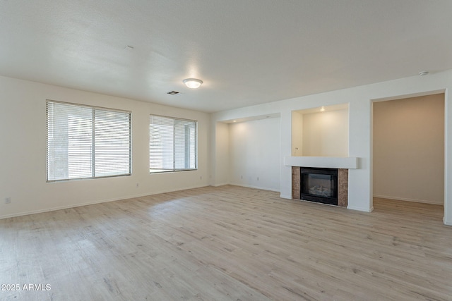 unfurnished living room with a tiled fireplace and light wood-type flooring