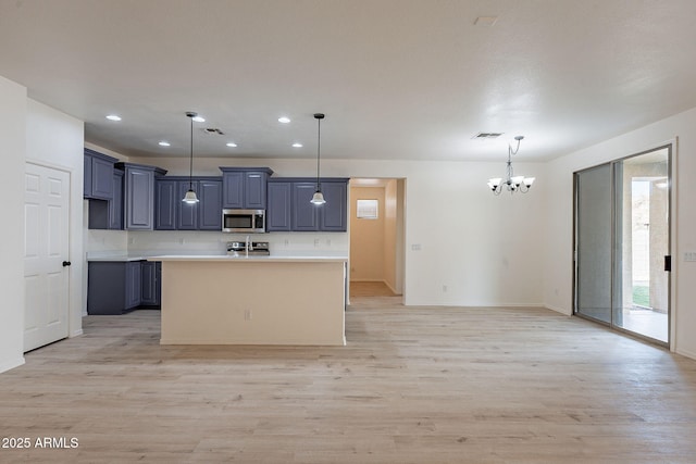 kitchen featuring stainless steel appliances, light hardwood / wood-style floors, an island with sink, and hanging light fixtures