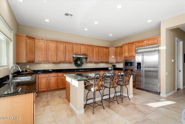 kitchen featuring dark stone countertops, a center island with sink, sink, and built in appliances