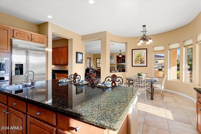 kitchen with built in appliances, sink, an inviting chandelier, decorative light fixtures, and an island with sink