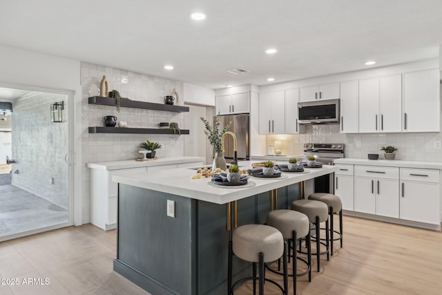 kitchen featuring appliances with stainless steel finishes, tasteful backsplash, an island with sink, white cabinets, and a kitchen bar