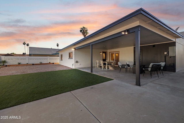 back house at dusk with a patio and a yard