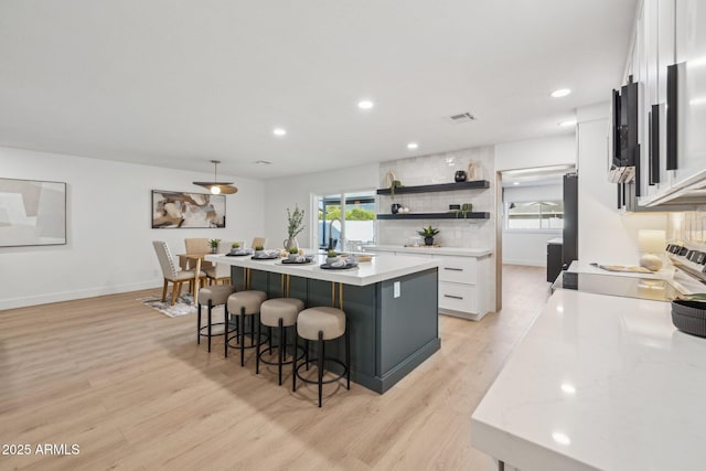 kitchen featuring pendant lighting, white cabinetry, a kitchen island, light hardwood / wood-style floors, and a kitchen bar