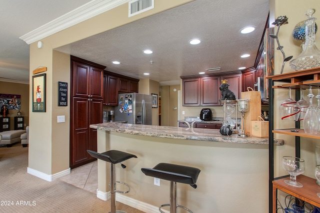 kitchen with kitchen peninsula, a breakfast bar area, light stone countertops, stainless steel refrigerator with ice dispenser, and light colored carpet