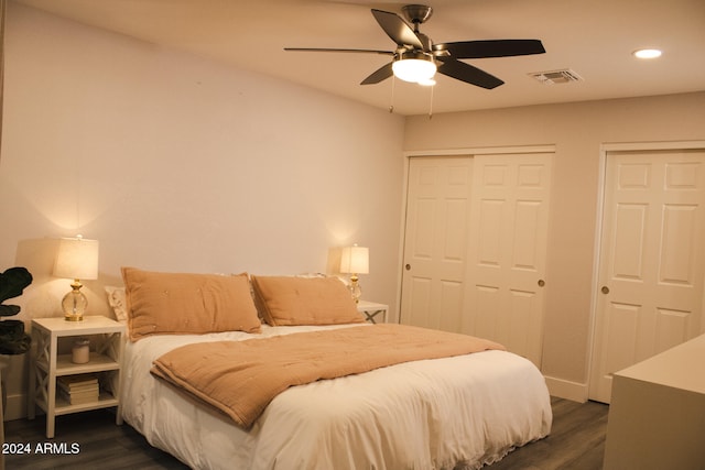 bedroom featuring ceiling fan, dark hardwood / wood-style flooring, and two closets