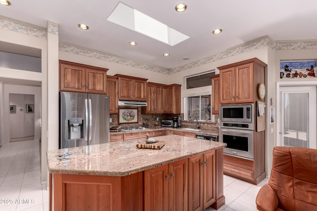 12803 W Amigo Dr, Sun City West, AZ 85375 - kitchen with stainless steel appliances, a skylight, light tile patterned floors, decorative backsplash, and light stone counters