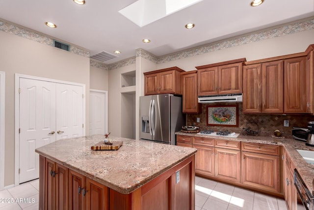 12803 W Amigo Dr, Sun City West, AZ 85375 - kitchen with stainless steel fridge with ice dispenser, under cabinet range hood, a skylight, brown cabinets, and light stone countertops