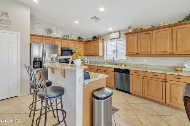 kitchen with a breakfast bar, stainless steel appliances, a center island, light stone counters, and vaulted ceiling