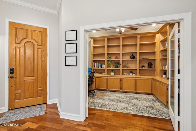 entrance foyer featuring crown molding, baseboards, built in desk, wood finished floors, and a ceiling fan