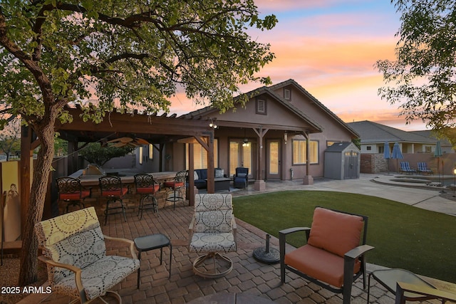 back of house at dusk featuring outdoor dry bar, a patio, fence, a storage shed, and an outdoor structure