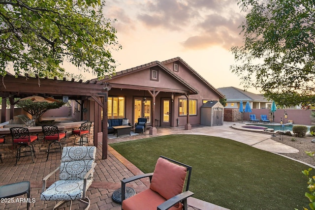 rear view of house featuring a lawn, outdoor lounge area, a patio area, a storage unit, and an outbuilding