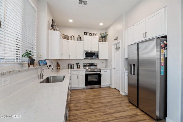 kitchen with sink, light stone countertops, light wood-type flooring, appliances with stainless steel finishes, and white cabinetry