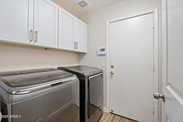 clothes washing area featuring washer and dryer, cabinets, and light hardwood / wood-style floors