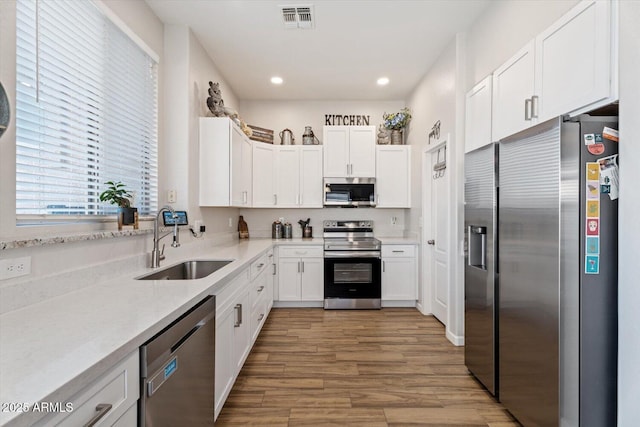 kitchen with white cabinets, sink, stainless steel appliances, and hardwood / wood-style floors