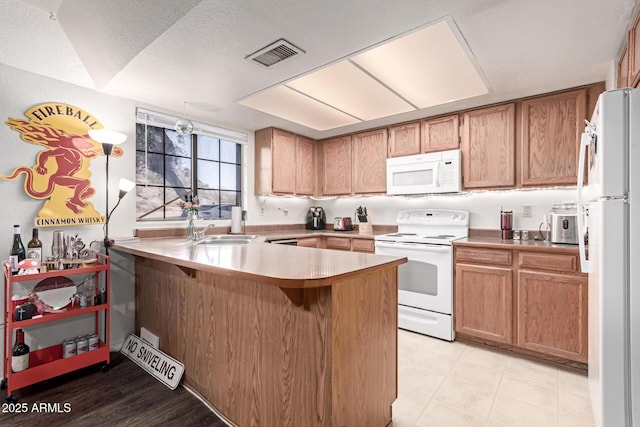 kitchen with a peninsula, white appliances, visible vents, light countertops, and brown cabinets