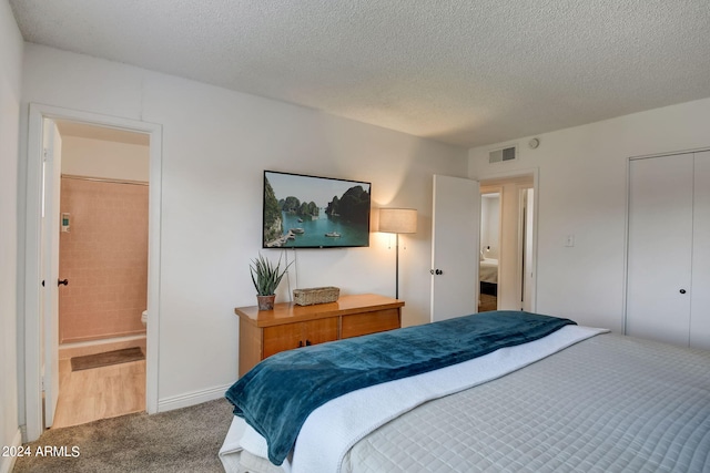 bedroom with a textured ceiling, visible vents, carpet floors, and connected bathroom