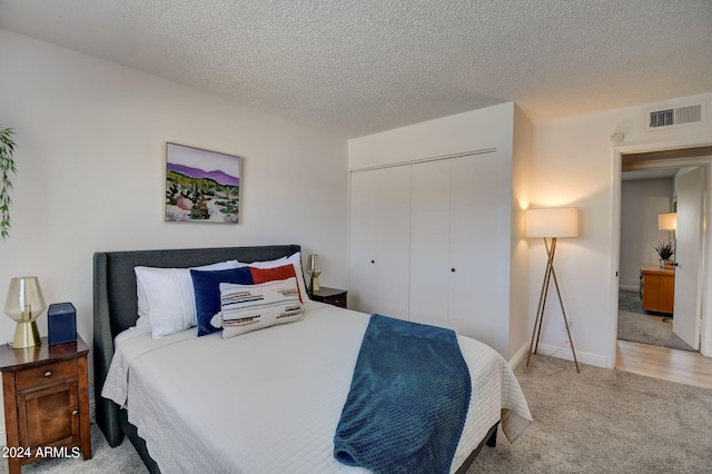 bedroom featuring a textured ceiling, visible vents, a closet, and light carpet