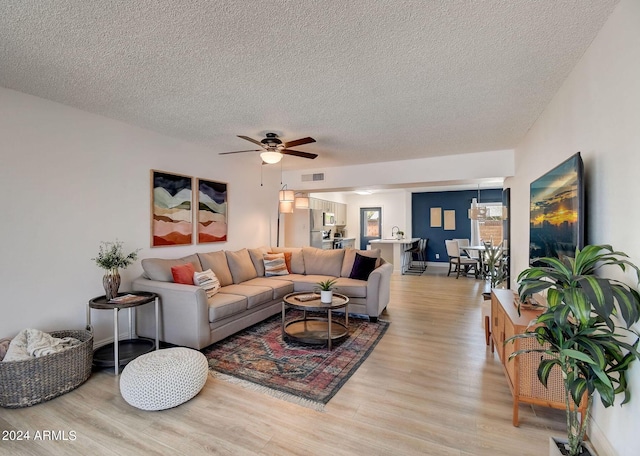 living room with light wood finished floors, visible vents, a textured ceiling, and a ceiling fan