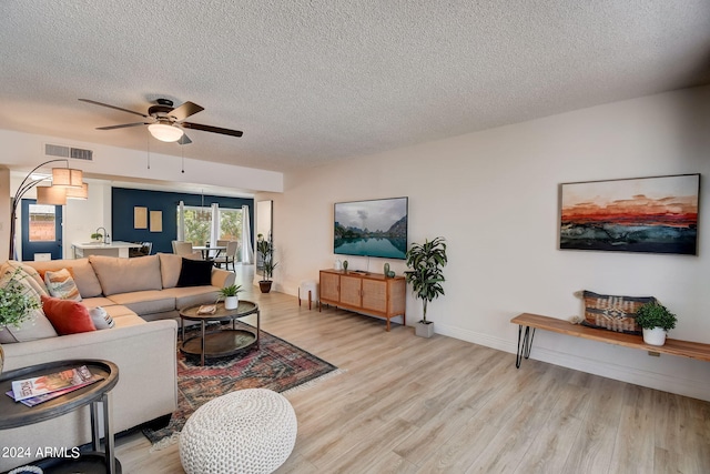 living area featuring a ceiling fan, visible vents, light wood finished floors, and a textured ceiling