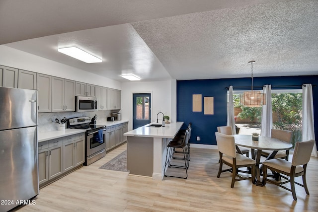 kitchen with gray cabinetry, a breakfast bar area, light wood-style flooring, appliances with stainless steel finishes, and a sink