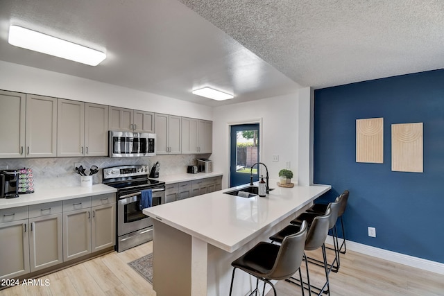 kitchen with a kitchen bar, gray cabinetry, a sink, tasteful backsplash, and stainless steel appliances