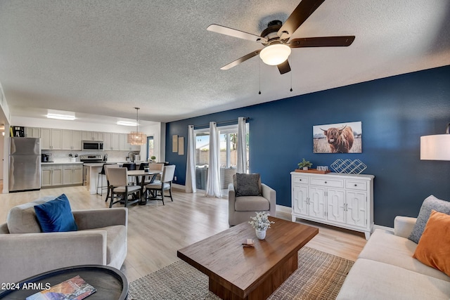 living room with baseboards, light wood-style floors, a ceiling fan, and a textured ceiling