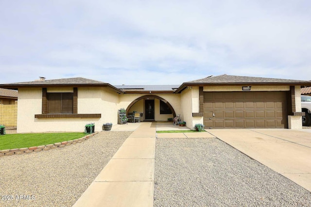 view of front of home with a garage, driveway, roof mounted solar panels, and stucco siding