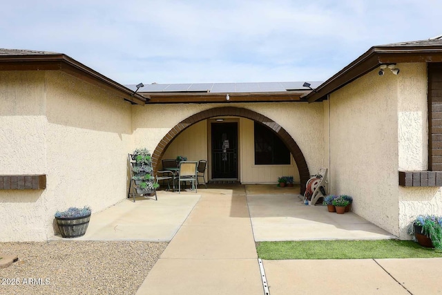 doorway to property with roof mounted solar panels, a patio, and stucco siding