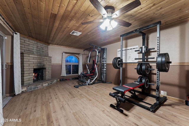 workout area with wood finished floors, a ceiling fan, a brick fireplace, wooden ceiling, and baseboards