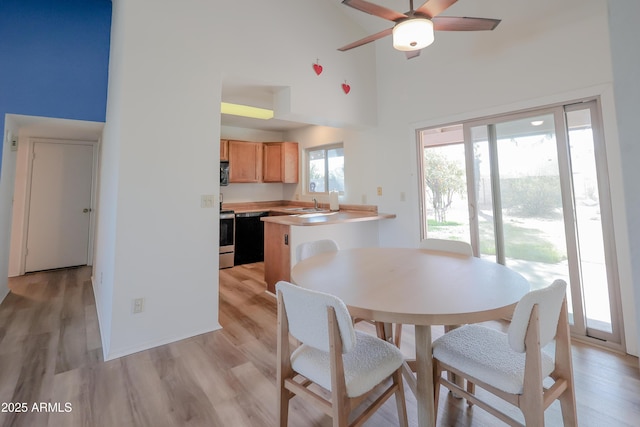 dining area featuring ceiling fan, sink, light hardwood / wood-style flooring, and a high ceiling