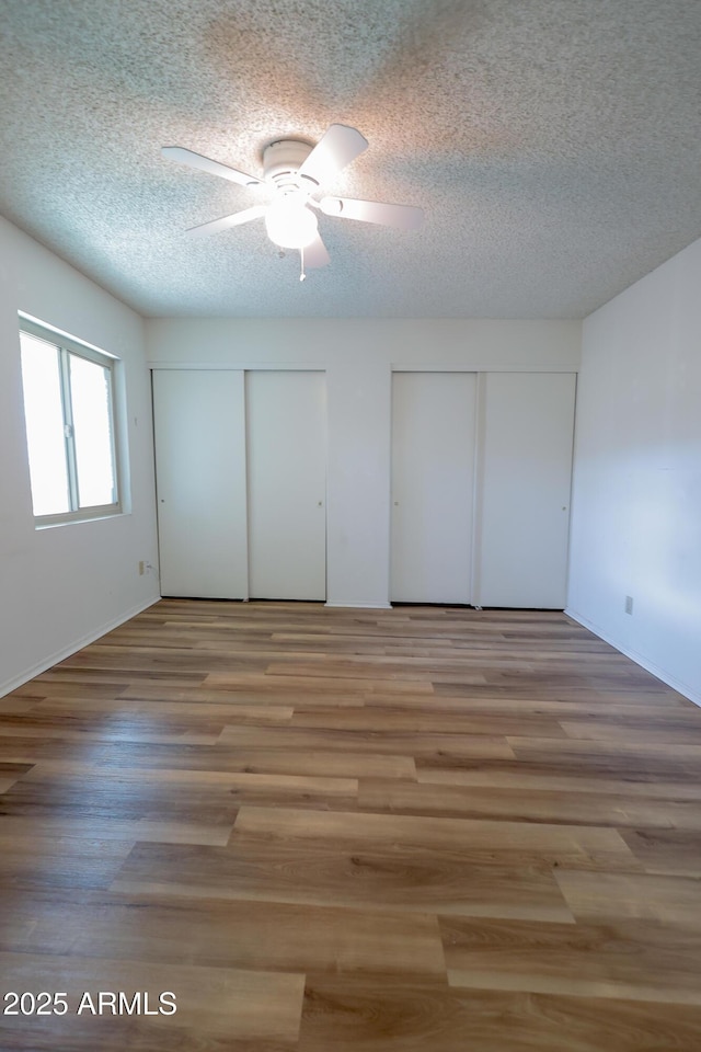 unfurnished bedroom with ceiling fan, hardwood / wood-style flooring, a textured ceiling, and multiple closets