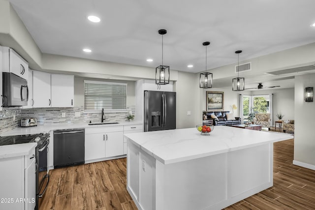 kitchen with pendant lighting, black appliances, sink, a kitchen island, and white cabinetry