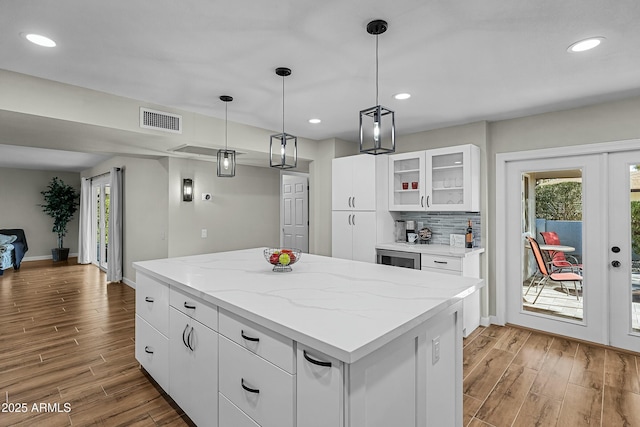 kitchen with french doors, hanging light fixtures, light stone countertops, a kitchen island, and white cabinetry