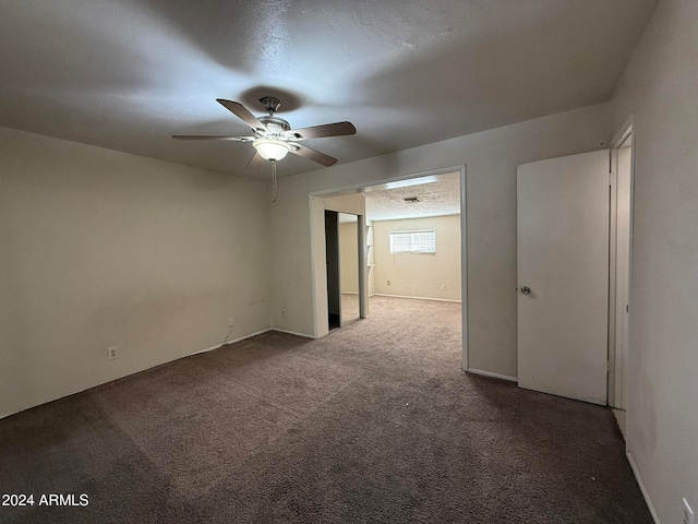 empty room featuring ceiling fan, a textured ceiling, and dark colored carpet