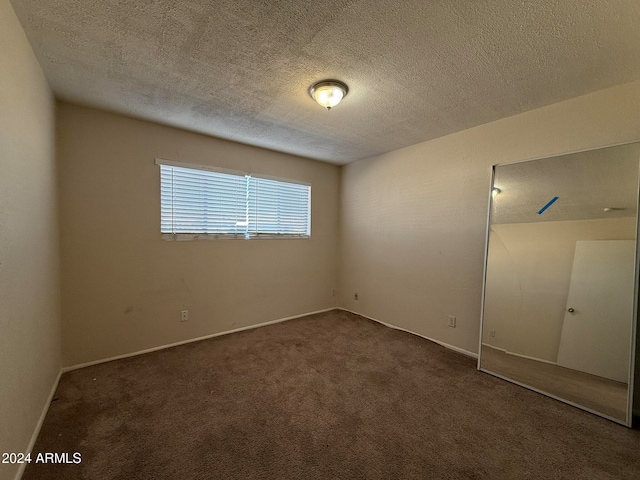 unfurnished room featuring a textured ceiling and dark carpet