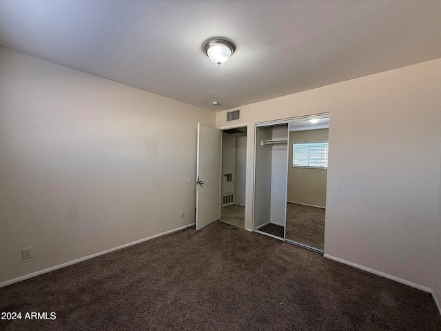 unfurnished bedroom with dark colored carpet and a closet