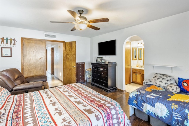 bedroom with visible vents, a ceiling fan, ensuite bath, wood finished floors, and arched walkways